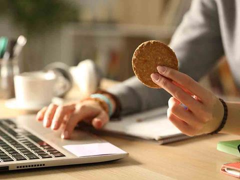 a person eating a cookie at a desk with a laptop on it
